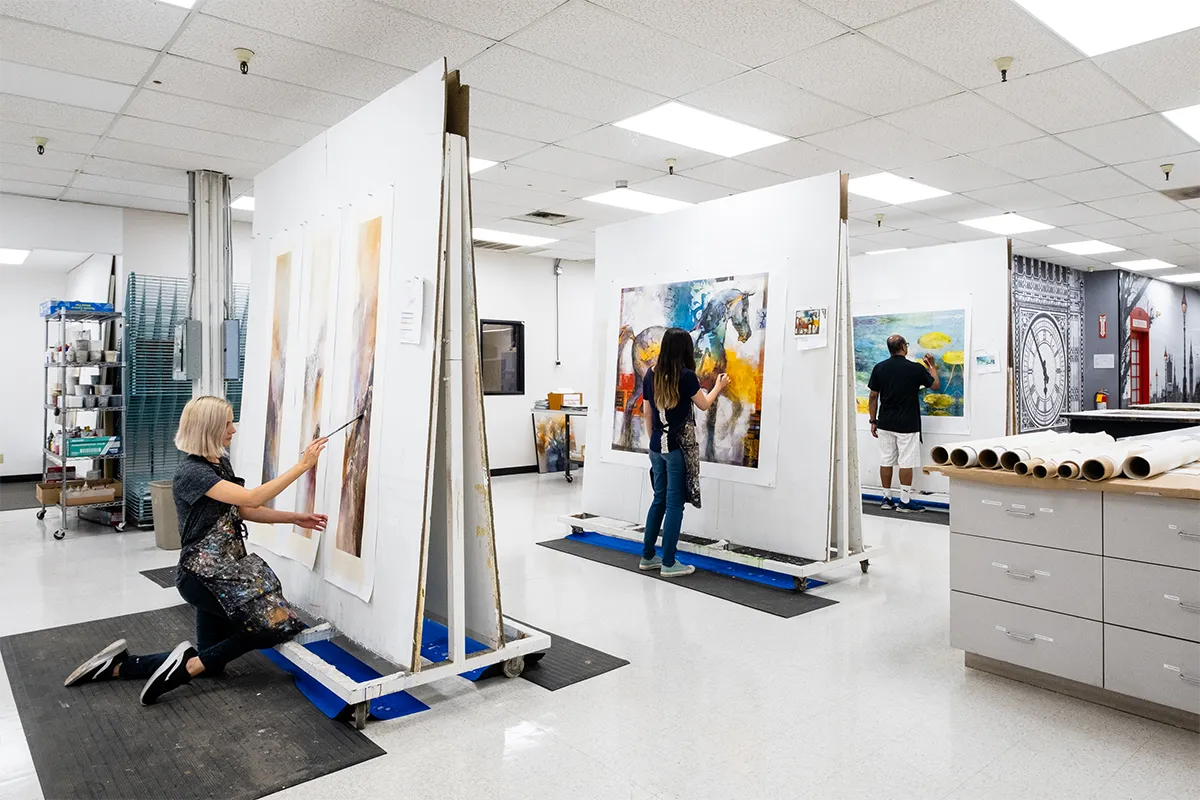 Artists embellishing printed artwork in a professional studio setting, adding hand-painted texture and detail to enhance large-scale canvas prints, demonstrating craftsmanship and artistic precision in a controlled production environment.